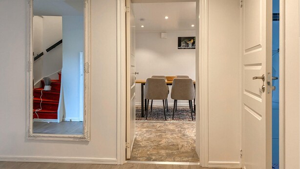 A hallway leading to a dining area with a table and chairs, a staircase with red steps, and a door with a blue frame. - 2 bedroom amazing apartment in Vimmerby (Vimmerby)