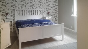 Une chambre à coucher avec un lit blanc, une table de chevet, une commode et un papier peint à motifs floraux.
