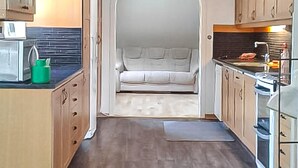 Une cuisine compacte avec des meubles en bois, un four à micro-ondes et une cuisinière. Un petit récipient vert est posé sur le comptoir.