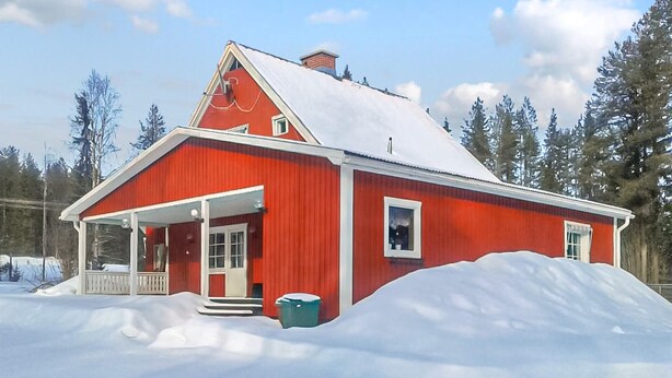 Une grange rouge avec un toit blanc, entourée de neige et d’arbres.