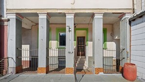 A building with a covered entrance, columns, and a staircase leading to a door with a green frame.