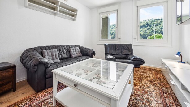 A living room with a black leather sofa, a glass coffee table, a white side table, and a patterned rug.
