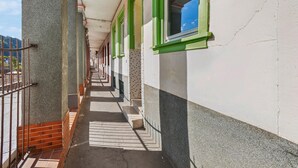 A corridor with a tiled floor, a brick wall on one side, and a white wall with green window frames on the other.