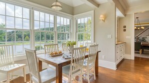 Un espace repas avec une grande table, des chaises blanches et une vue sur un lac, visible à travers de grandes fenêtres.