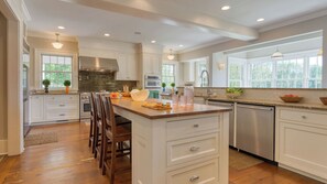 A modern kitchen with white cabinetry, a central island, and a large window providing natural light.