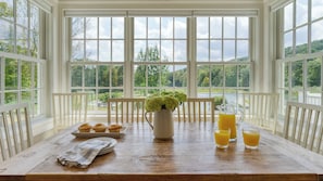 A breakfast table with muffins, a pitcher of flowers, and glasses of orange juice.