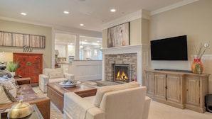 A living room with a fireplace, a television, and a kitchen in the background. - Secluded Estate Optional Guest House, Pond, Playroom, Gym & Theater Sunny Pond by Avantstay (Austerlitz)