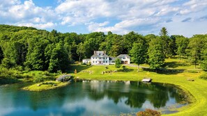 Une grande maison avec un étang devant, entourée d’arbres.