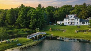 Une grande maison avec un étang, un pont et une pelouse.