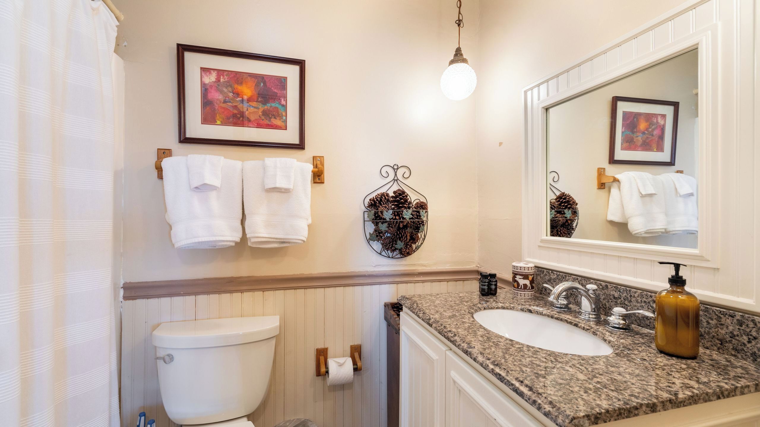 A bathroom with a toilet, sink, and two framed artworks on the wall.