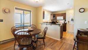 A spacious kitchen with wooden cabinets, a central island, and a dining area with wooden chairs. - Ash Vale by Avantstay Expansive Deck + Ping Pong + Covered Porch Blue Ridge Mountain Escape (Mars Hill)