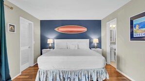 A bedroom with a large bed, two bedside tables with lamps, a blue accent wall, and a framed picture on the wall. - 3C Mariners Walk by Avantstay Beach & Pool Access, Enclosed Porch (Isle of Palms)
