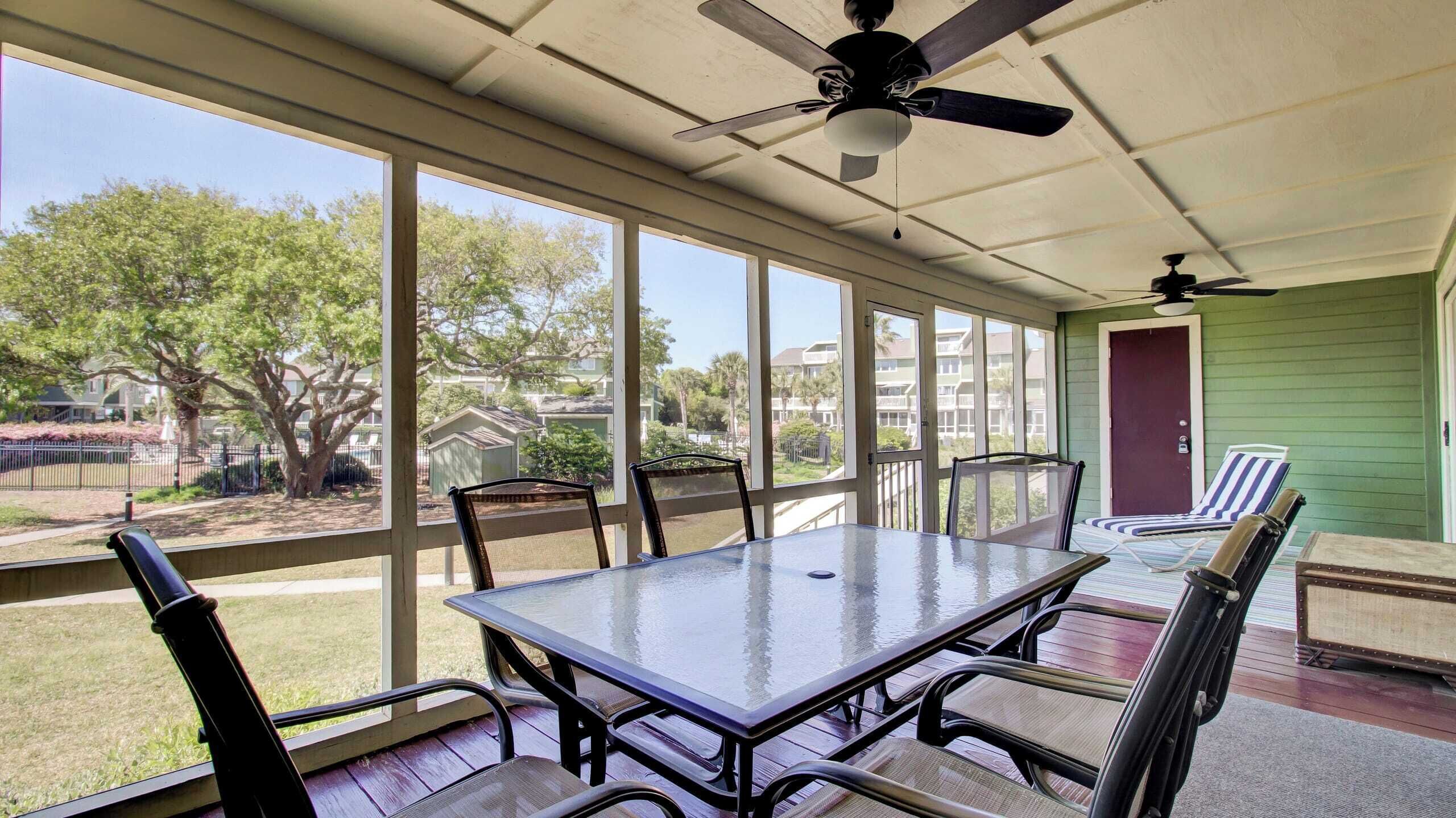 A covered patio with a table and chairs, large windows, and a ceiling fan.