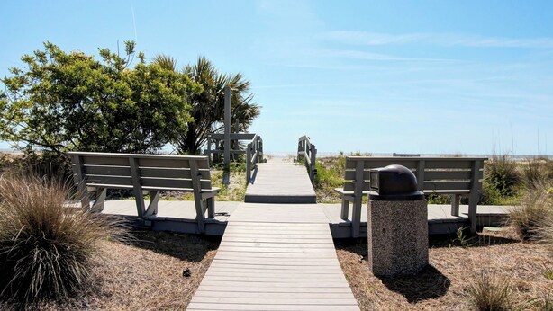 A wooden boardwalk leading to a beach with benches and a trash can. - 3C Mariners Walk by Avantstay Beach & Pool Access, Enclosed Porch (Isle of Palms)