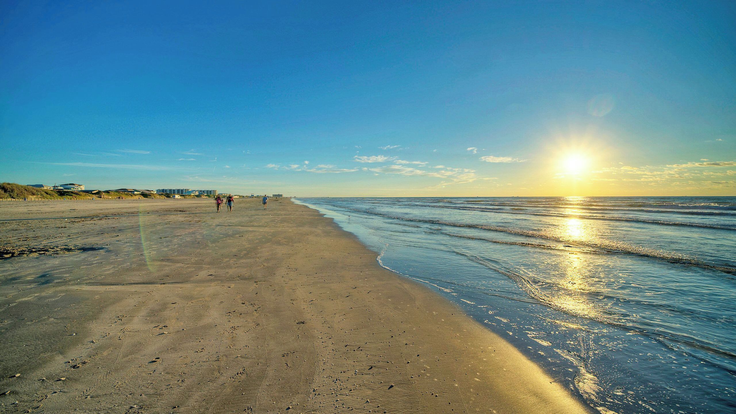 Une plage avec un ciel dégagé, un coucher de soleil et quelques personnes qui se promènent.