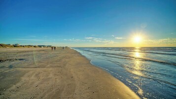 Una playa con cielo despejado, un atardecer y algunas personas caminando.