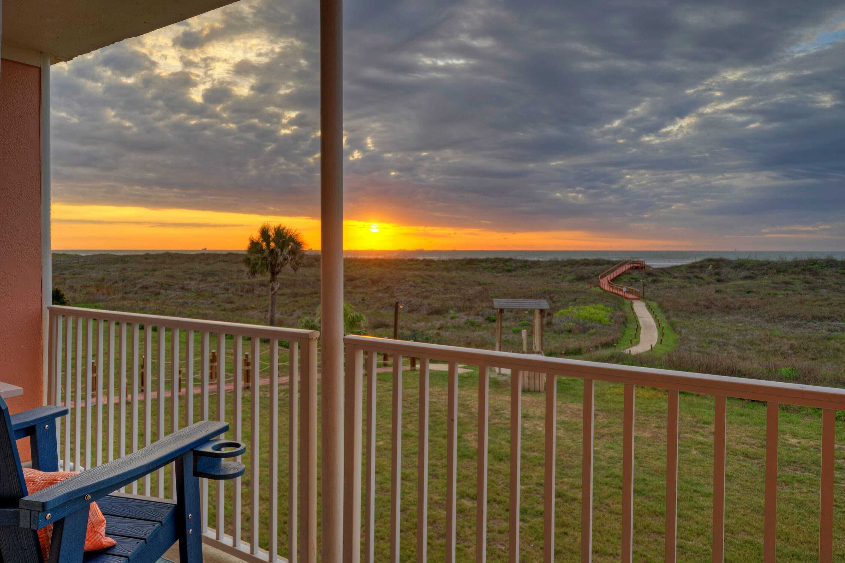 A balcony with a view of a sunset over a dune landscape.