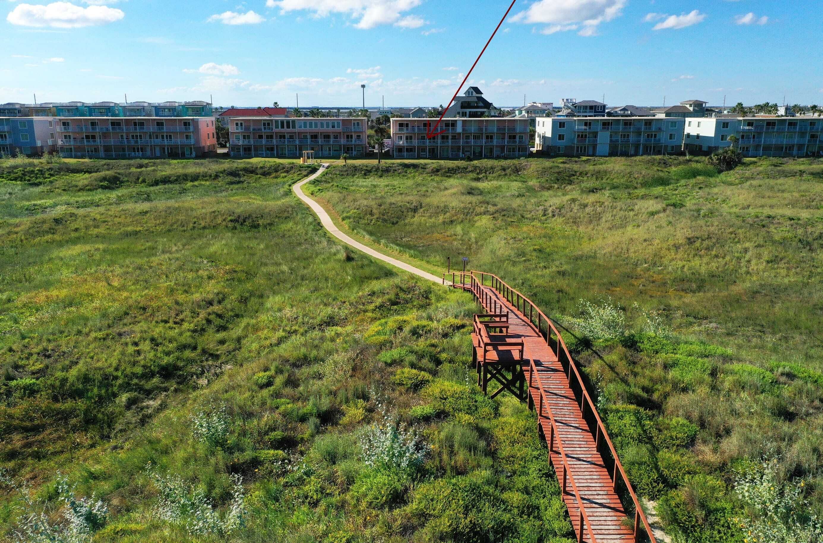 A red pedestrian bridge over a grassy field leading to a row of multi-story buildings.