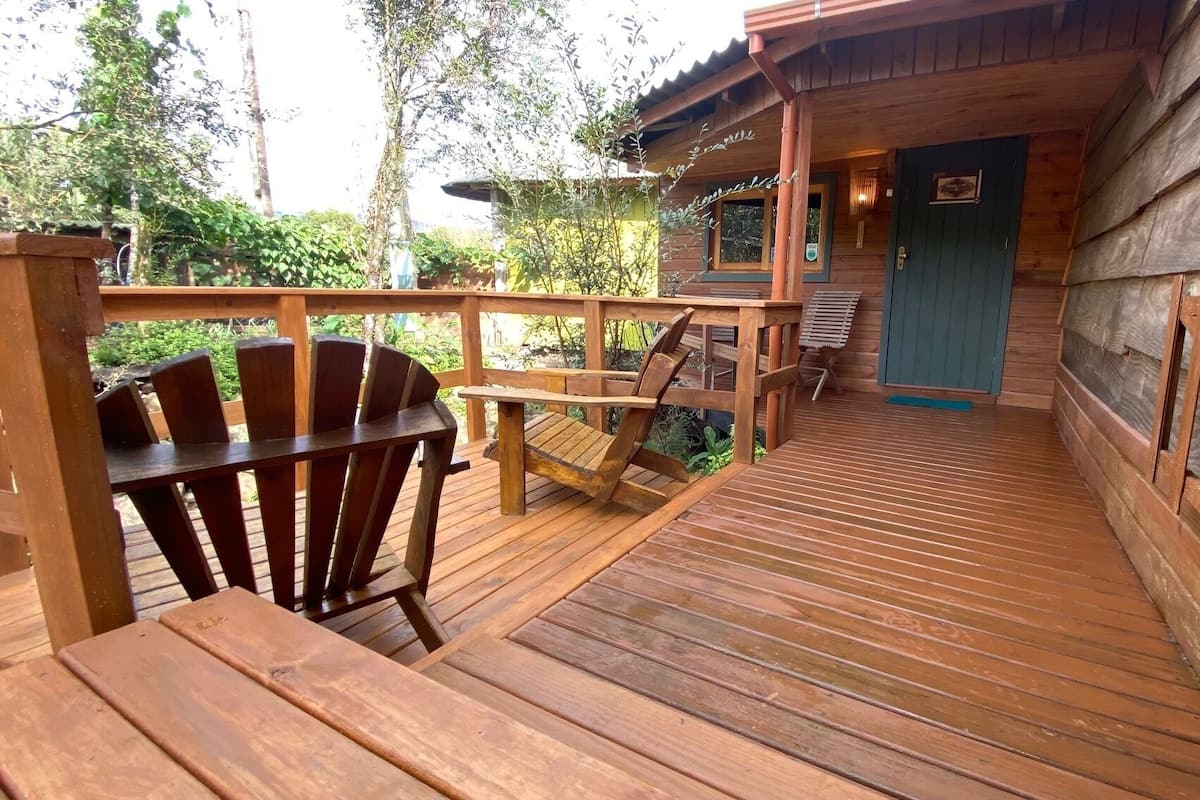 Eine Holzdar Terrasse mit einem Holzstuhl und einem Tisch, die zu einem Gebäude mit einer blauen Tür führt.