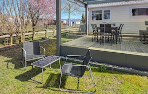 A covered outdoor seating area with chairs and a table, a deck with a table and chairs, and a house in the background.