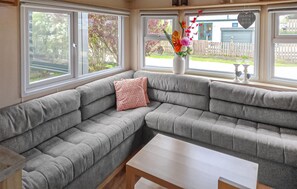 A corner sectional sofa with a white coffee table, large windows, and a vase with flowers.