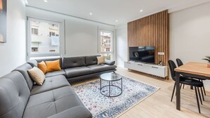A modern living room with a grey sectional sofa, a small round coffee table, a wooden TV stand, and a dining table with chairs.