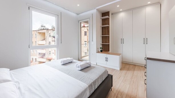 A modern bedroom with a large bed, built-in wardrobe, and a view of the city.