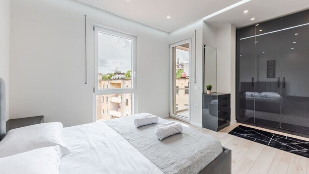 Un dormitorio moderno con una cama grande, un vestidor y un balcón con puerta corrediza de vidrio.