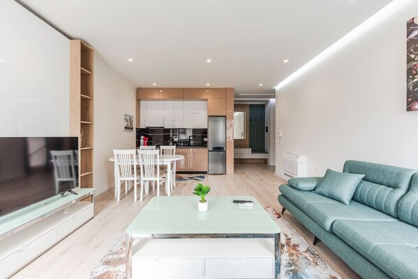 Een moderne woonkamer met een televisie, een bank, een eettafel en een keuken op de achtergrond.