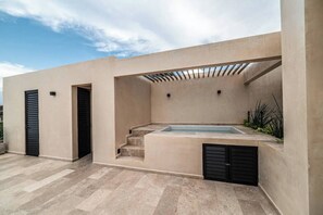 A modern outdoor pool area with a concrete deck, a built-in hot tub, and a pergola structure.