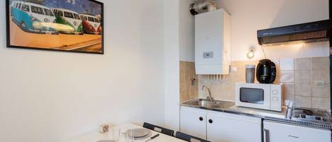 A compact kitchen with a microwave, sink, and a small refrigerator. A dining table with chairs is set up in front of the kitchen.