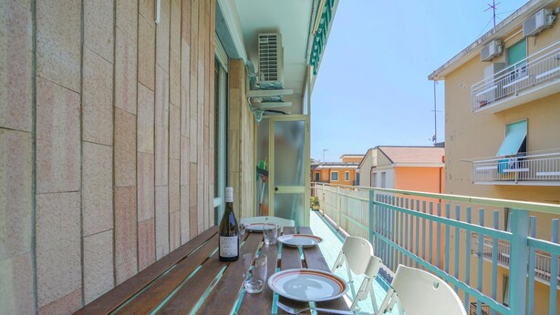 A balcony with a wooden table set for dining, a bottle of wine, and a chair. - 2 bedroom nice apartment in Cavi di Lavagna (Cavi di Lavagna)
