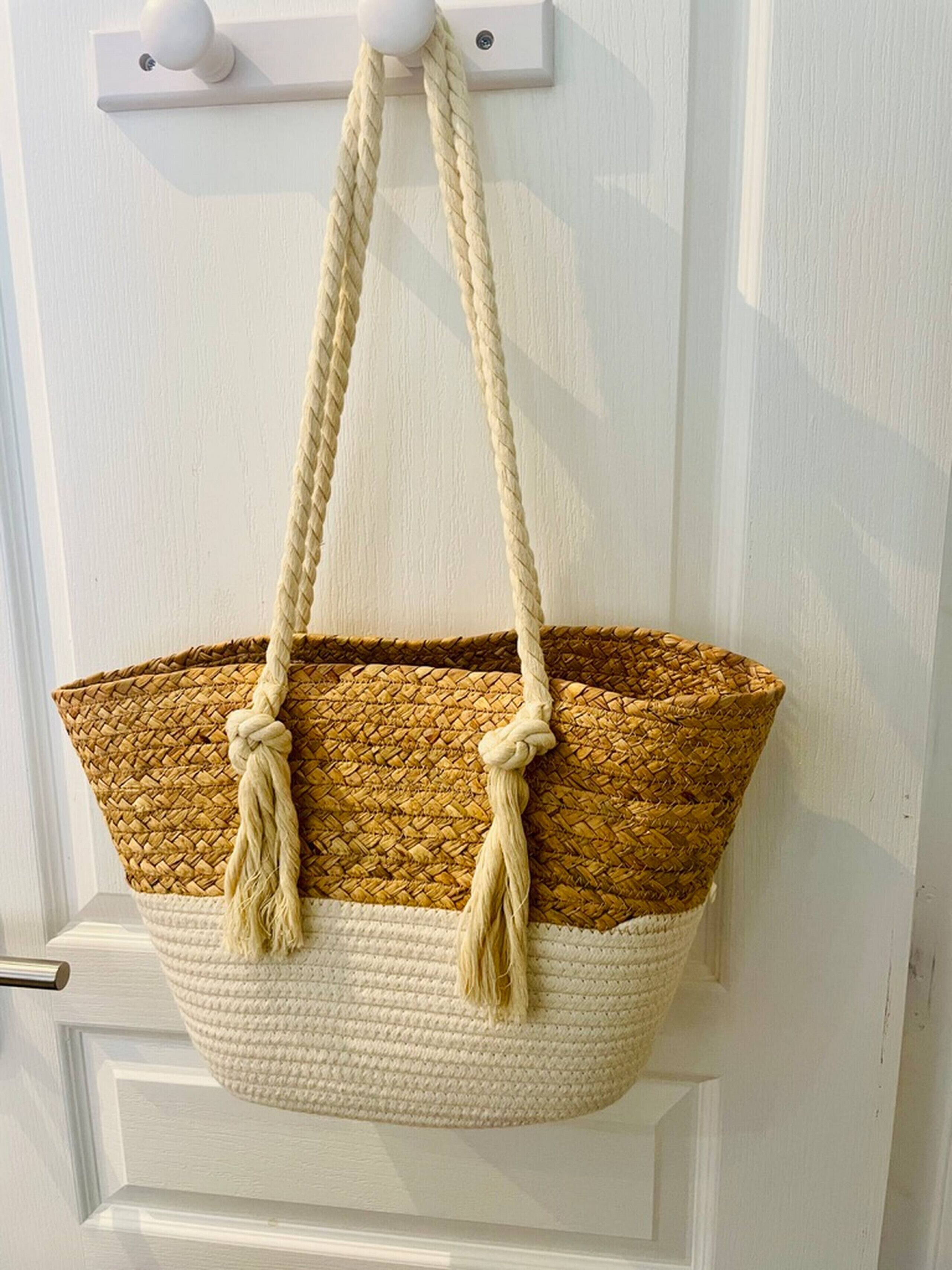 A woven basket bag with a handle hanging on a white door.