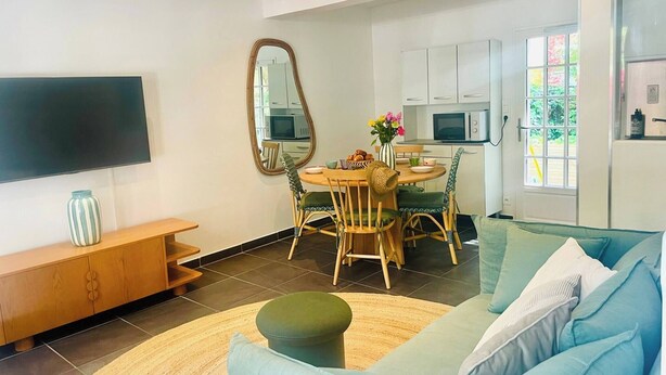 Una sala de estar moderna con televisor de pantalla plana, un comedor con mesa redonda y una cocina con gabinetes blancos.