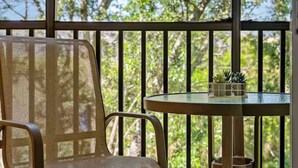 A chair and a small table with a plant on a balcony with a railing and greenery in the background. - Family Friendly Condo near Disney (Davenport)