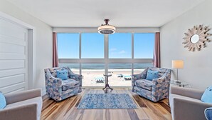 Une pièce dotée d’une grande fenêtre donnant sur une plage, de deux fauteuils à motifs, d’une petite table ronde et d’un lampadaire.