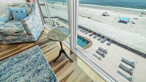 Une pièce dotée d’une grande fenêtre donnant sur une plage, une piscine et un coin salon avec un canapé à motifs et une petite table.