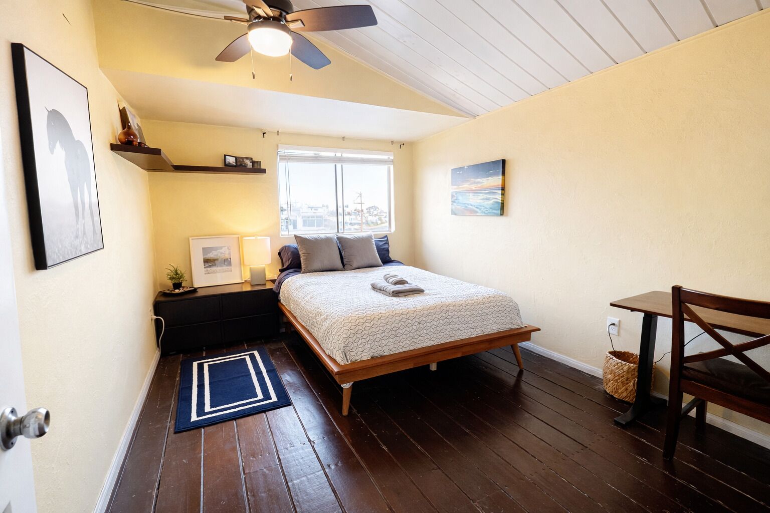 Une chambre à coucher comprenant un lit, un bureau, une chaise, un ventilateur de plafond et une fenêtre.