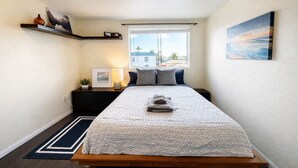 Une chambre à coucher comprenant un lit, une table de chevet, une fenêtre avec vue, une étagère avec des objets décoratifs et un tableau au mur.