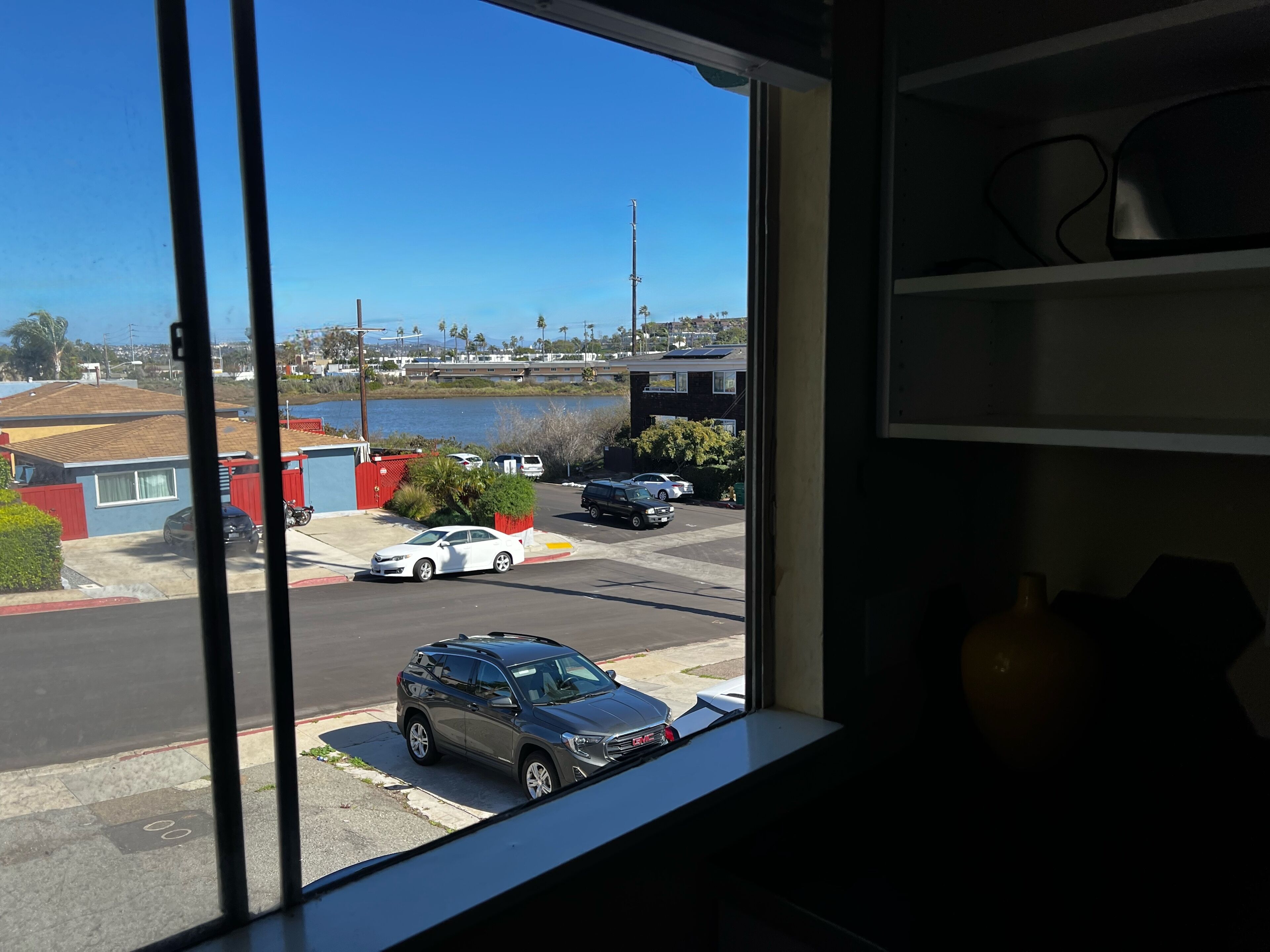 A view from a window overlooking a parking lot with cars, a small building, and a body of water.