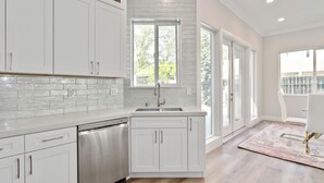 A modern kitchen with white cabinetry, a stainless steel dishwasher, and a large window providing natural light.