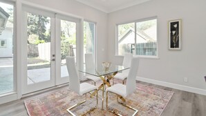 A dining area with a glass table, white chairs, and a patterned rug.