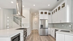 A modern kitchen with white cabinetry, stainless steel appliances, and a wooden floor.