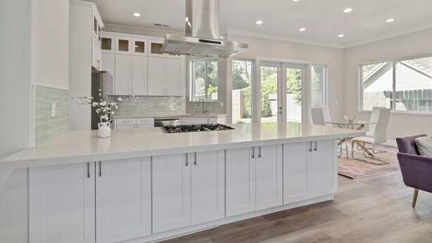 A modern kitchen with white cabinetry, a central island, stainless steel appliances, and a large window providing natural light.