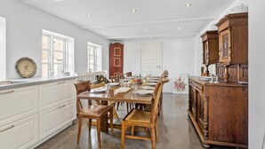 Una cocina amplia con una gran mesa de comedor dispuesta para seis personas, armarios de madera y vistas al exterior a través de las ventanas.