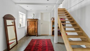 Un pasillo con una escalera de madera, un espejo grande, un armario de madera y una alfombra roja.