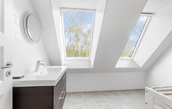 Un baño moderno con tragaluz, un lavamanos blanco y un mueble de madera oscura.