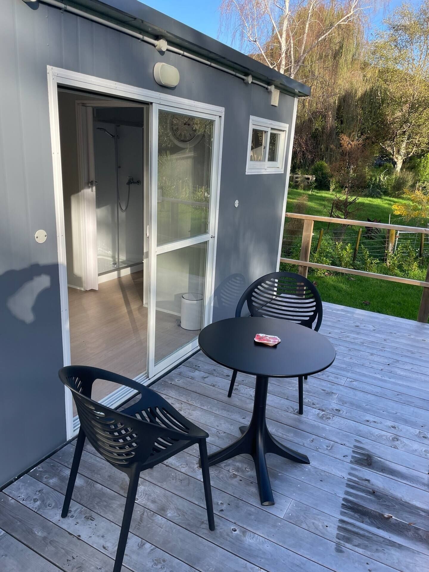 Il s’agit d’un bâtiment compact et moderne, doté d’une porte-fenêtre coulissante qui donne accès à un espace douche. Une petite terrasse abrite une table ronde et deux chaises.