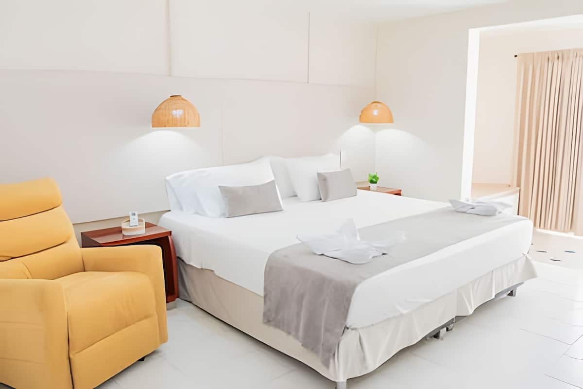 Ein Hotelzimmer mit einem Bett, einem gelben Sessel, zwei Nachttischlampen und einer kleinen Pflanze auf dem Nachttisch.