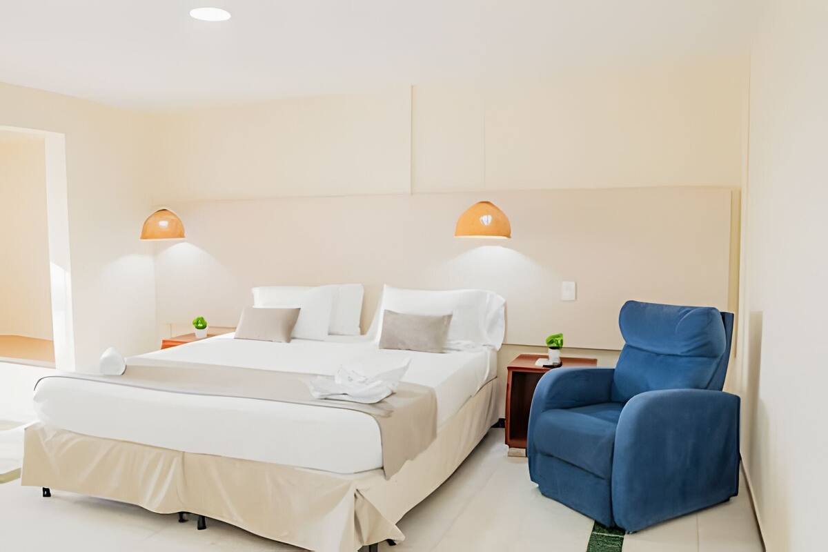 Ein Hotelzimmer mit einem Bett, zwei Nachttischen, einem blauen Sessel und zwei Wandlampen.